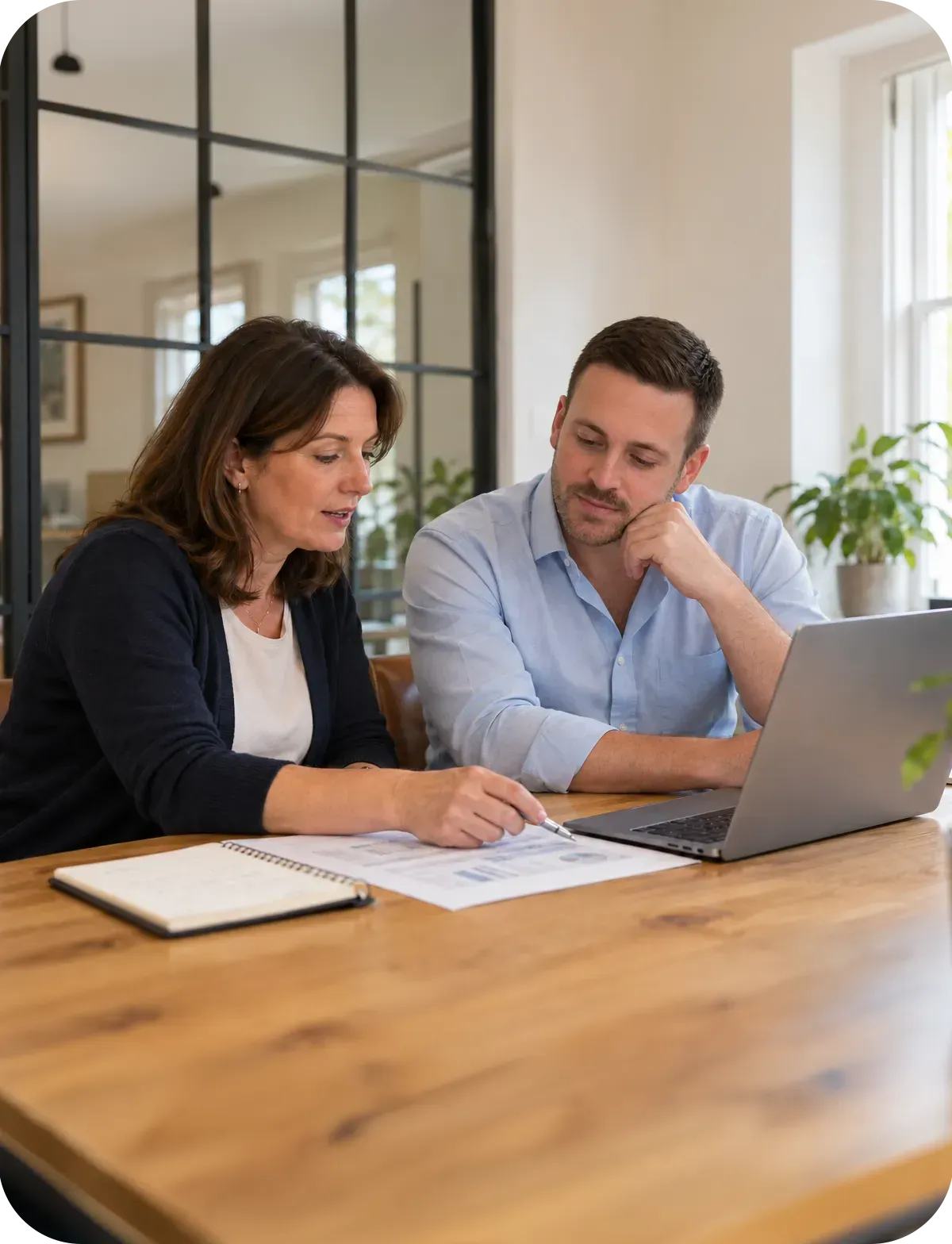 Two colleagues reviewing financial reports together beside a laptop in a bright, modern office.