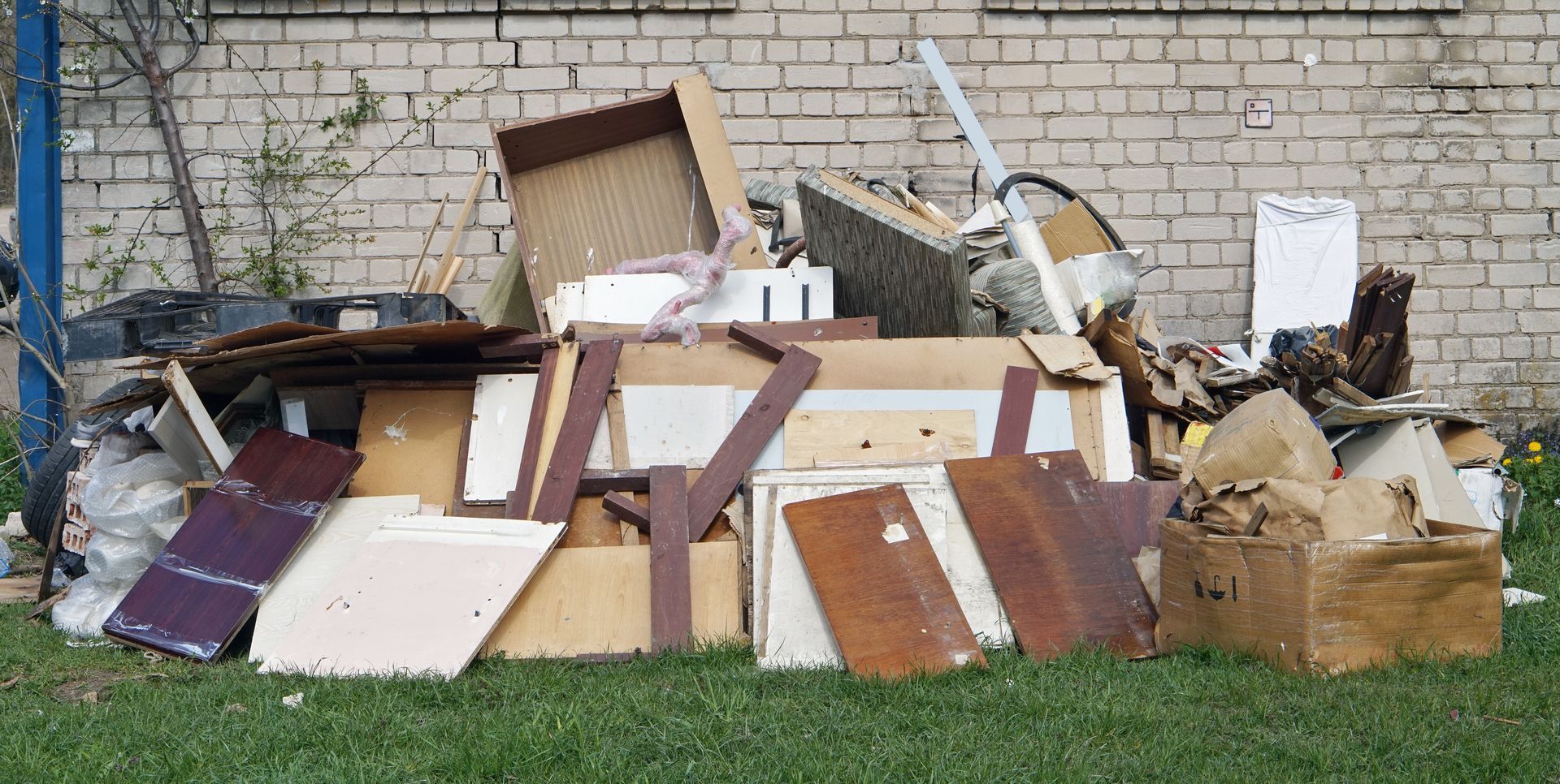 Piles of discarded furniture and cardboard boxes piled against a brick wall outdoors