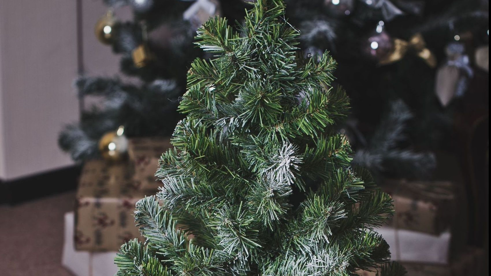 A small christmas tree is sitting in a wooden bucket filled with logs.