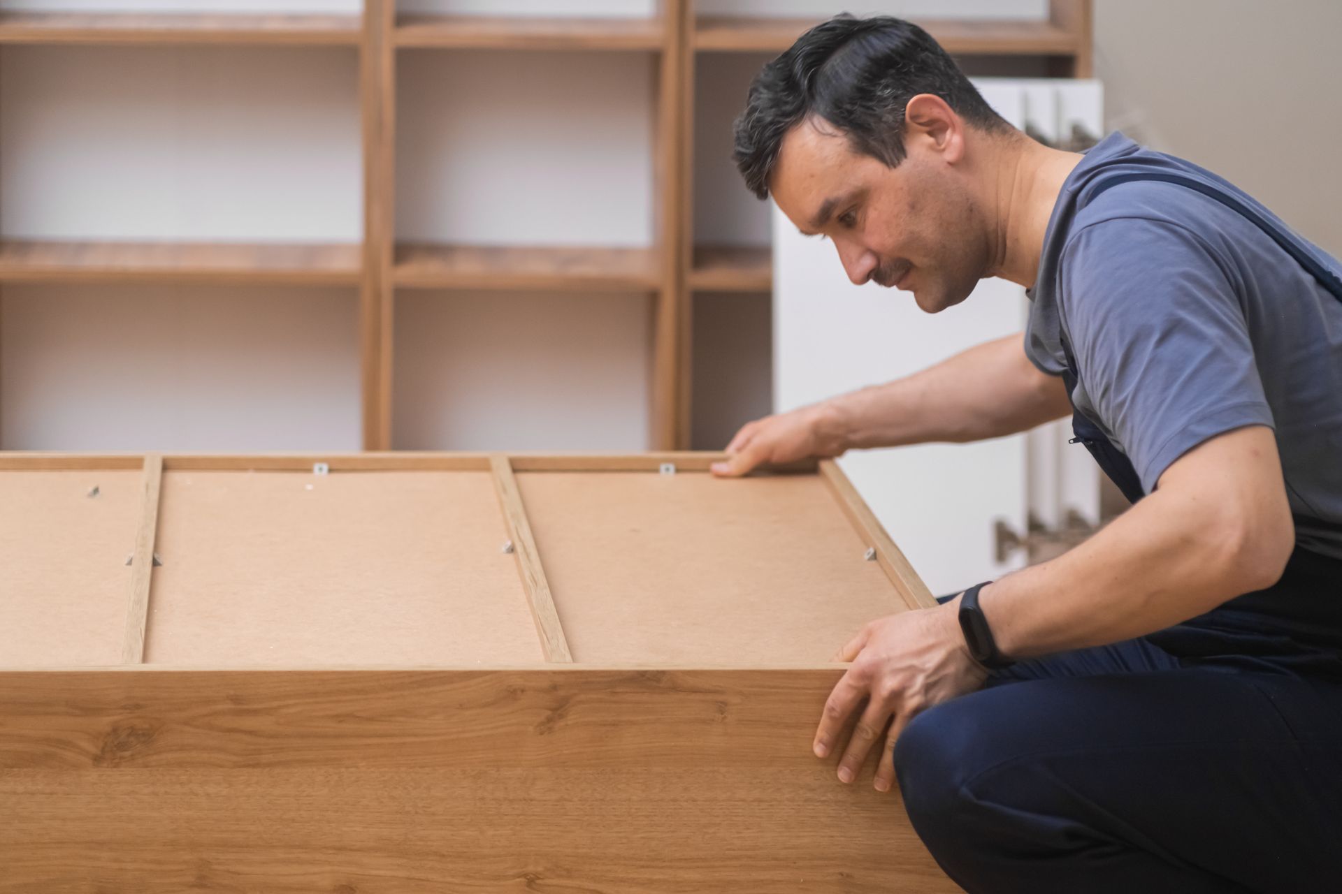 A man is kneeling down and working on a piece of wood.