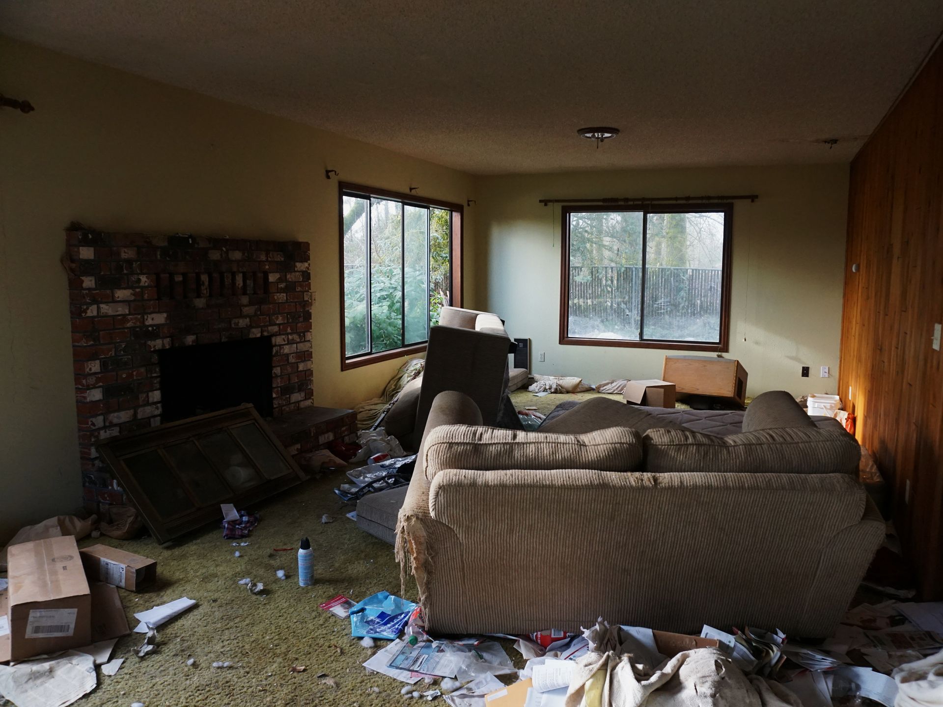 A living room in an abandoned house with a couch , chairs , and fireplace.