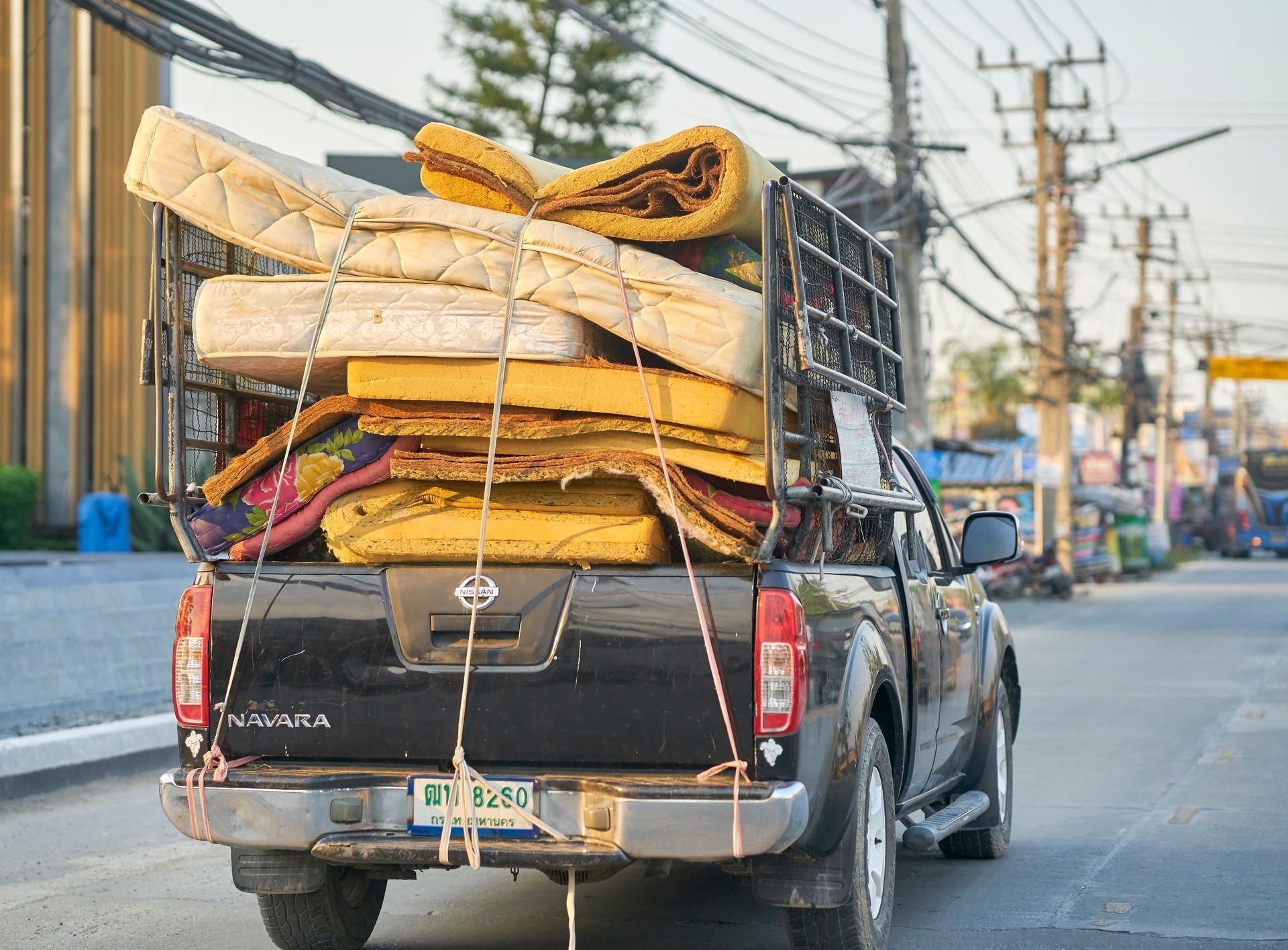 A truck with a stack of mattresses in the back is driving down a street.
