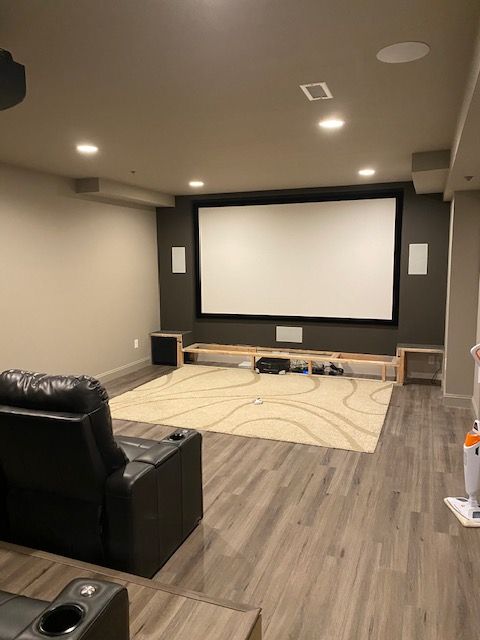 Home theater room with a large projection screen, recliner seating, and wood-look flooring