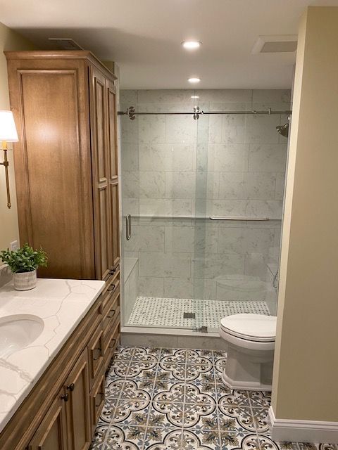 Bathroom with vanity, toilet, patterned tile floor, and glass-enclosed shower.