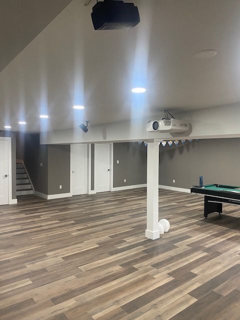 Empty recreation room with wood-look flooring, white support column, ceiling lights, and a pool table at right