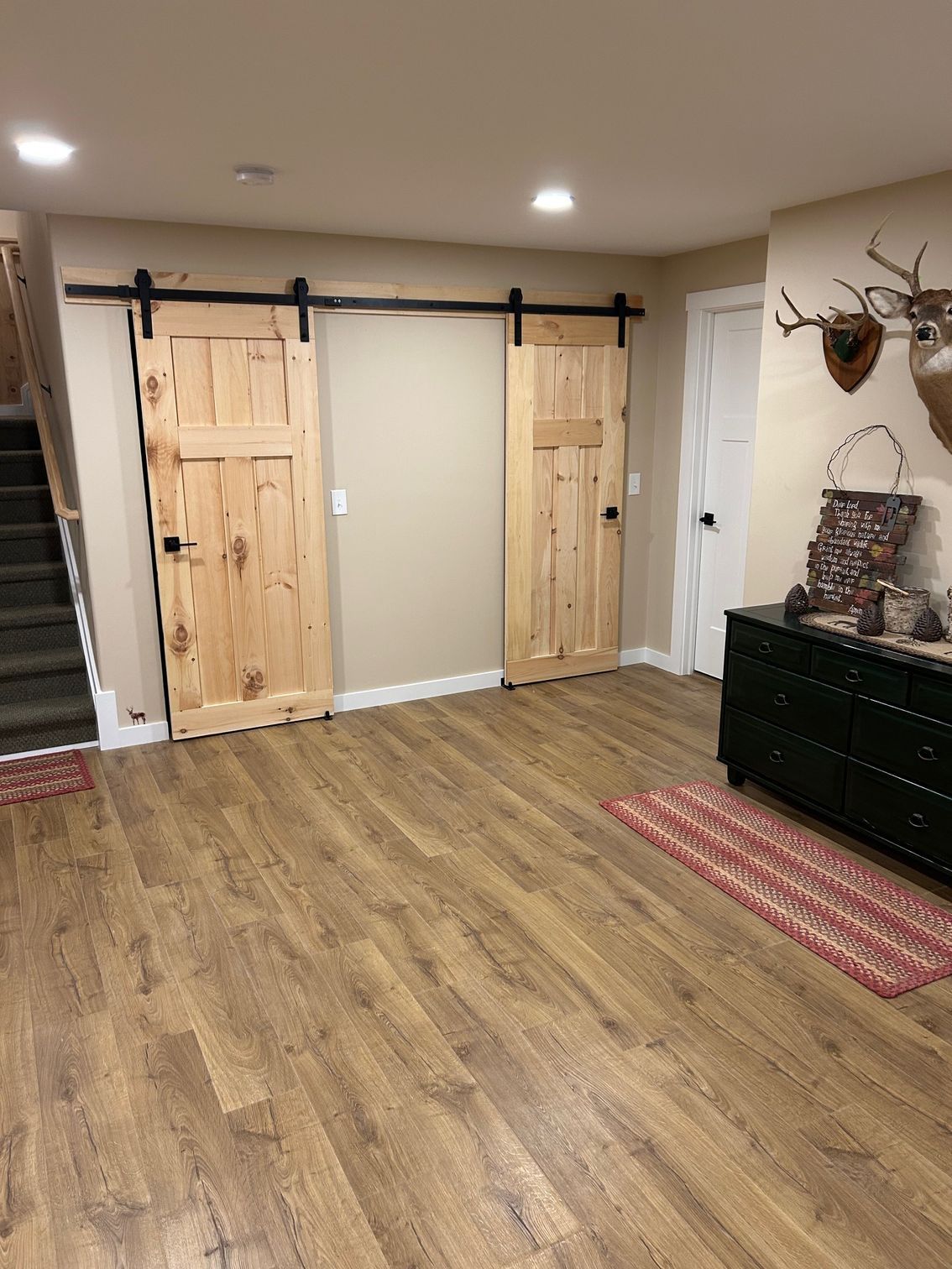Basement room with wood flooring, sliding barn doors, and a black dresser with wall decor.