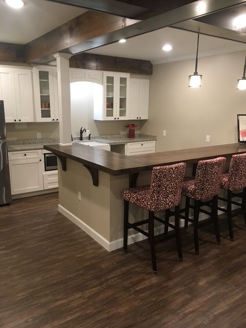 Modern kitchen with a large island, white cabinets, and dark wood flooring, with three patterned bar stools.