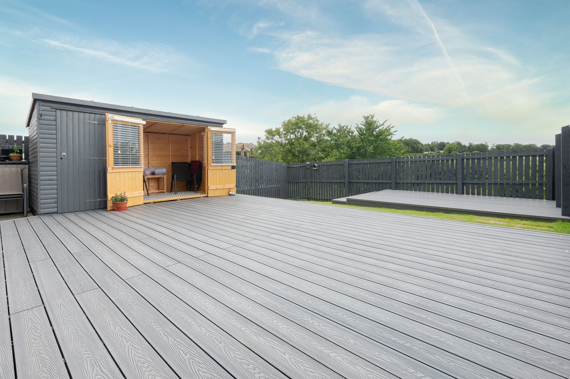 A wooden shed is sitting on top of a wooden deck next to a fence.