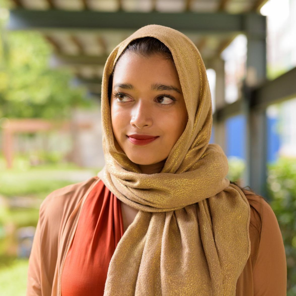 A woman is smiling with her eyes closed in a park.