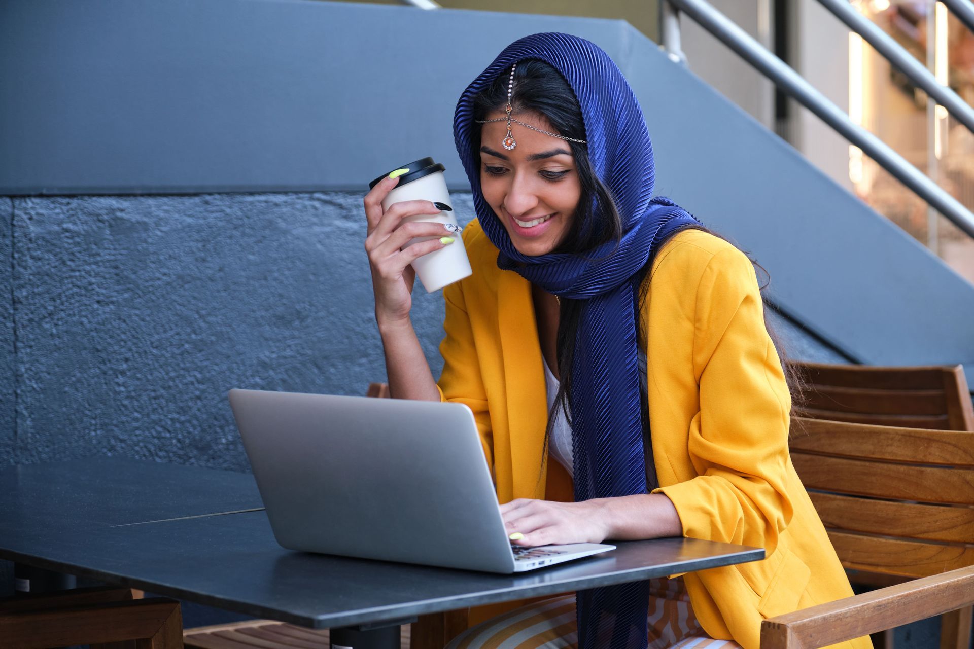 A woman is sitting at a table with a laptop and a cup of coffee.