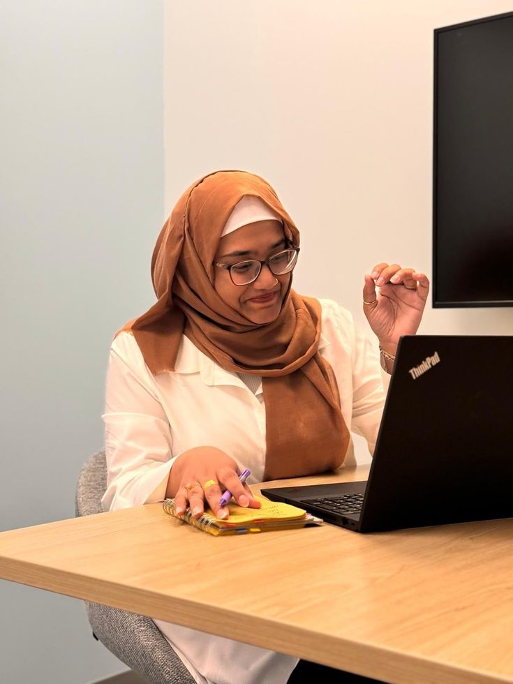 A woman in a hijab is sitting at a table using a laptop computer.