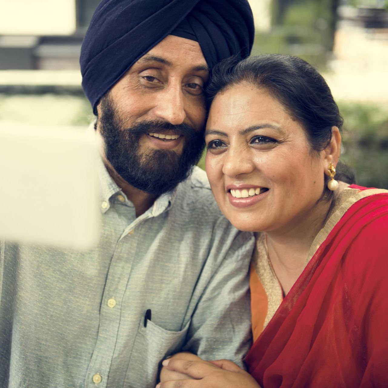 A man wearing a turban is hugging a woman in a red dress