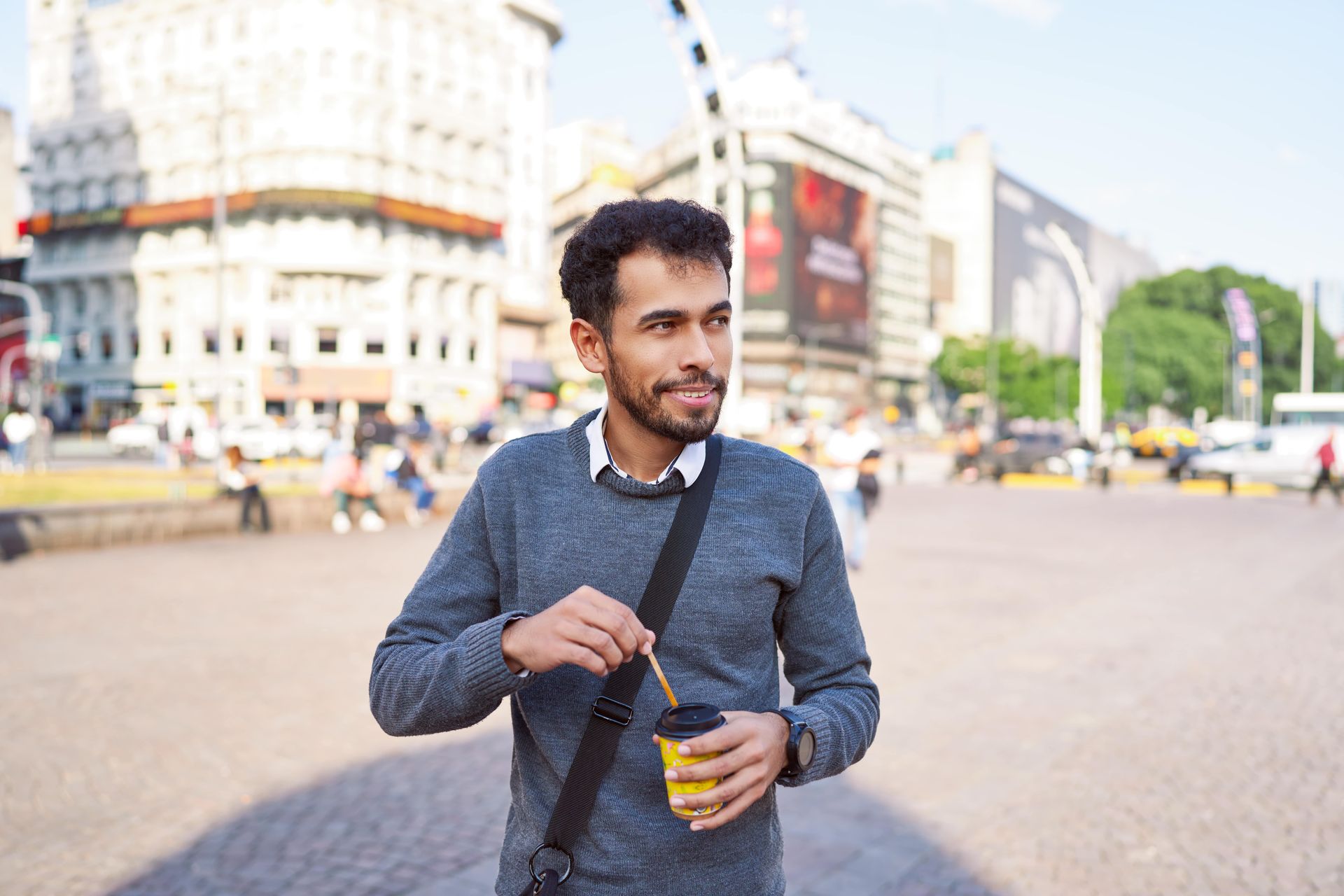 A man is standing on a city street holding a cup of coffee.