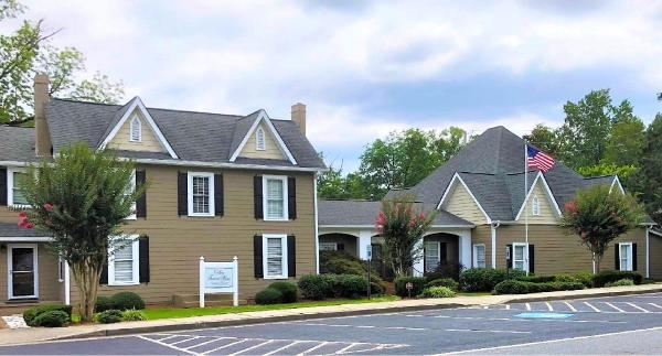 Two-story brick and tan buildings with a parking lot and a flag in front under a cloudy sky