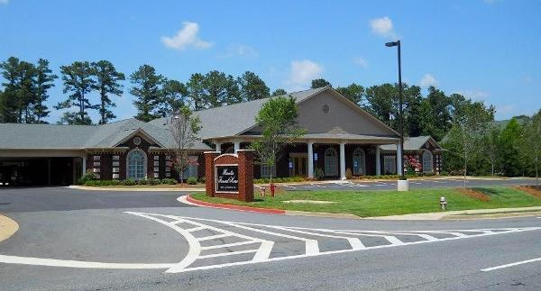 Single-story brick building with covered entrance, parking area, and landscaped sign by a roundabout.