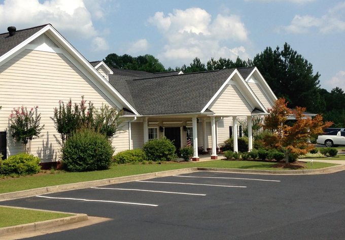 Single-story beige house with white trim beside an empty parking lot on a sunny day