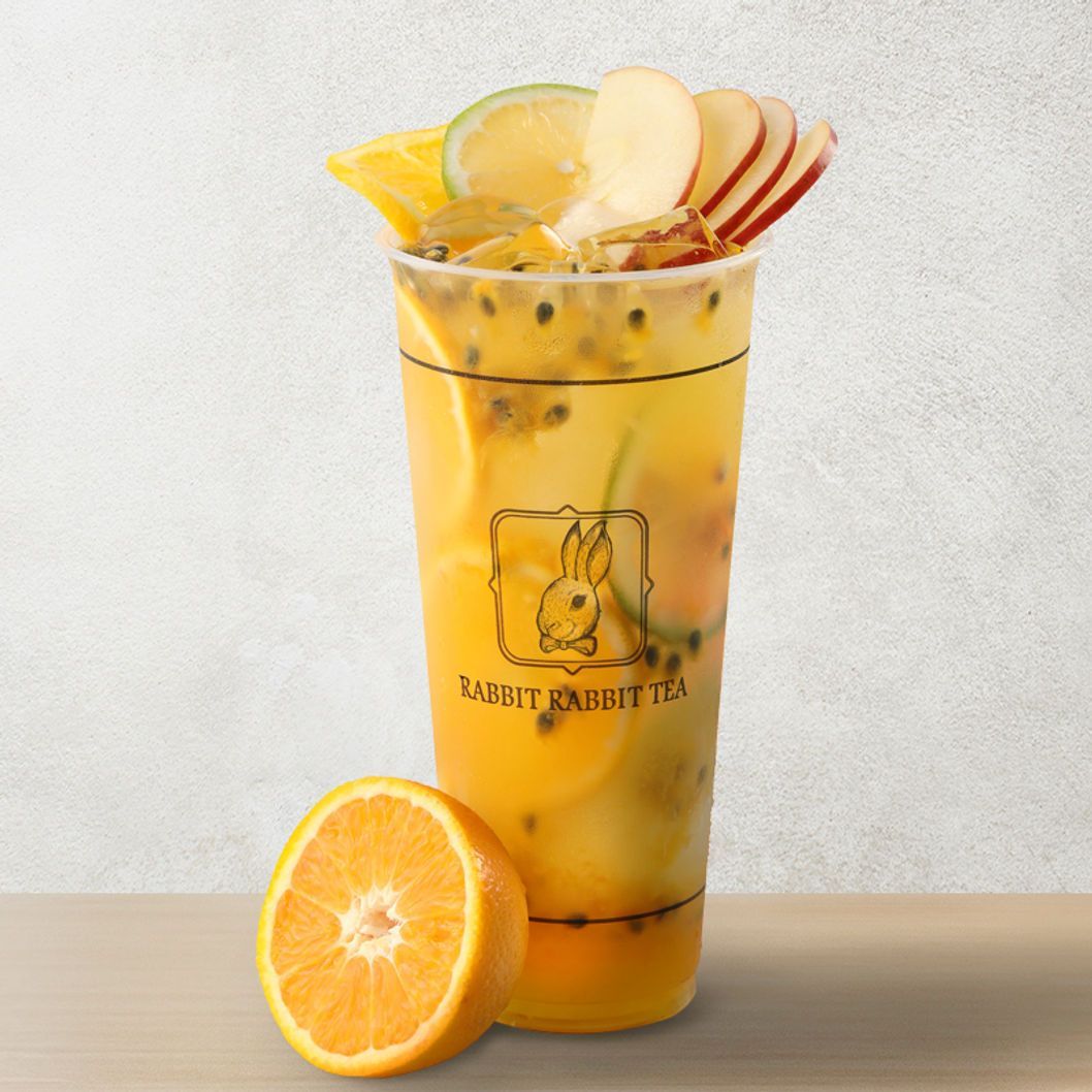 Orange fruit drink in a clear cup with ice, lemon and apple slices, and a halved orange beside it.