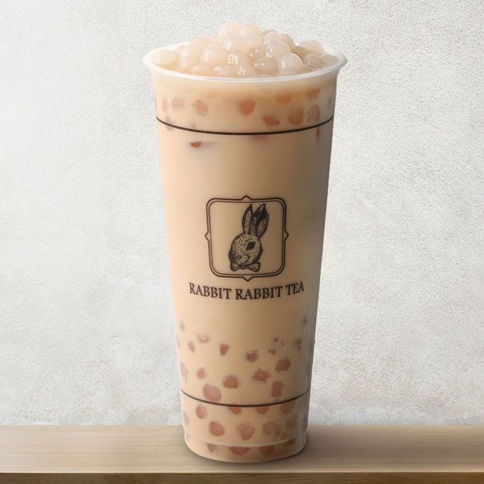 Clear plastic cup of milk tea with tapioca pearls and rabbit logo on a light background