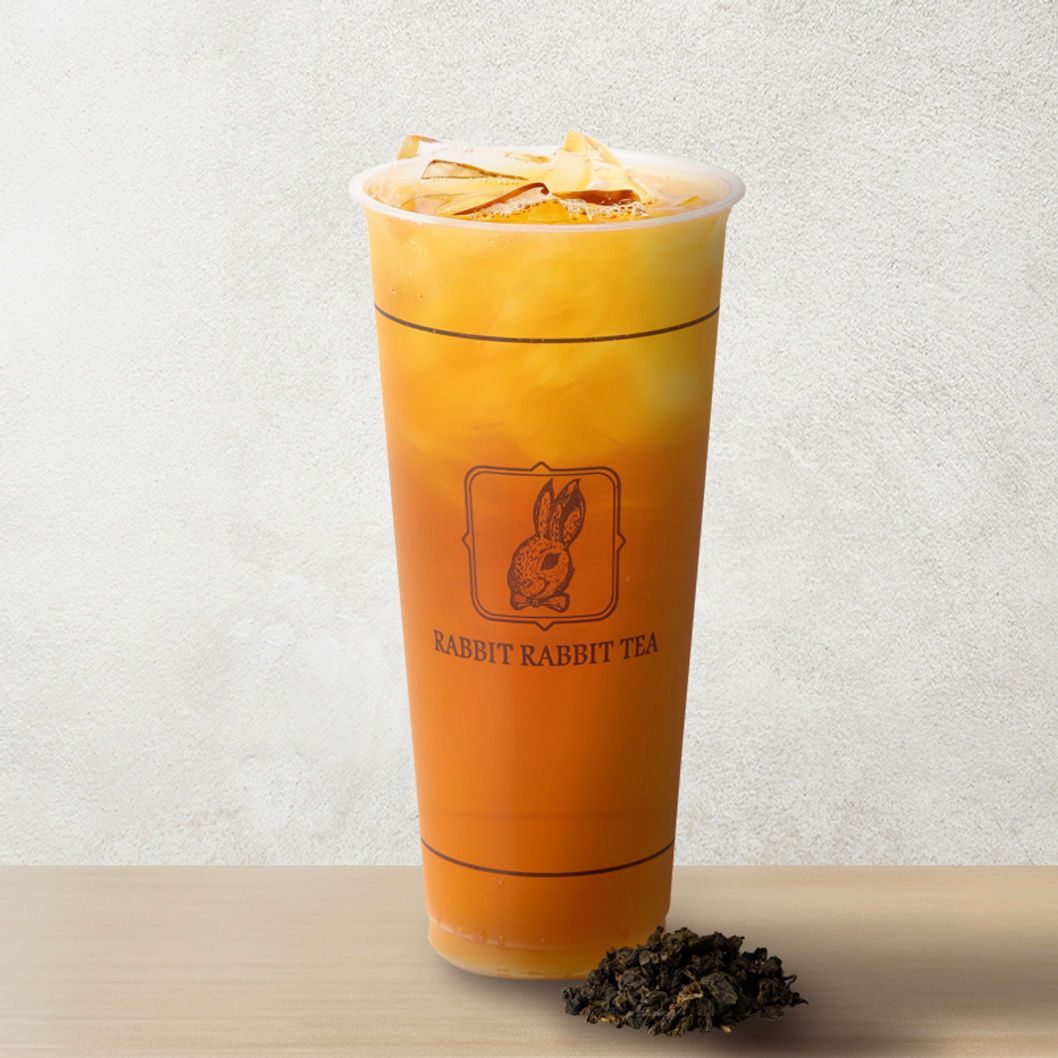 Tall orange iced tea in a clear cup on a table, with lemon slices and loose tea leaves beside it