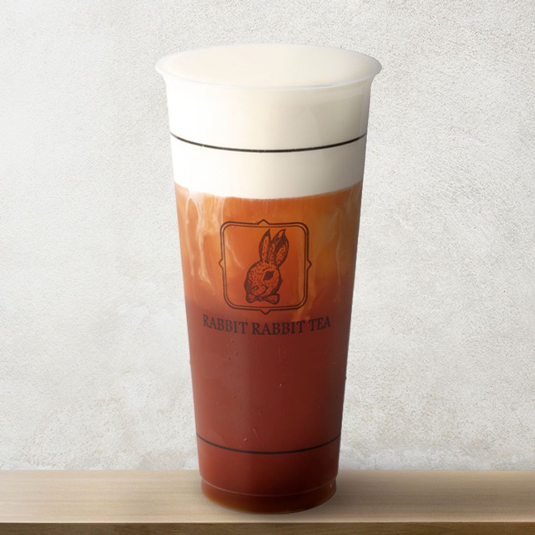 Tall clear cup of reddish drink with a white lid on a wooden surface against a gray background