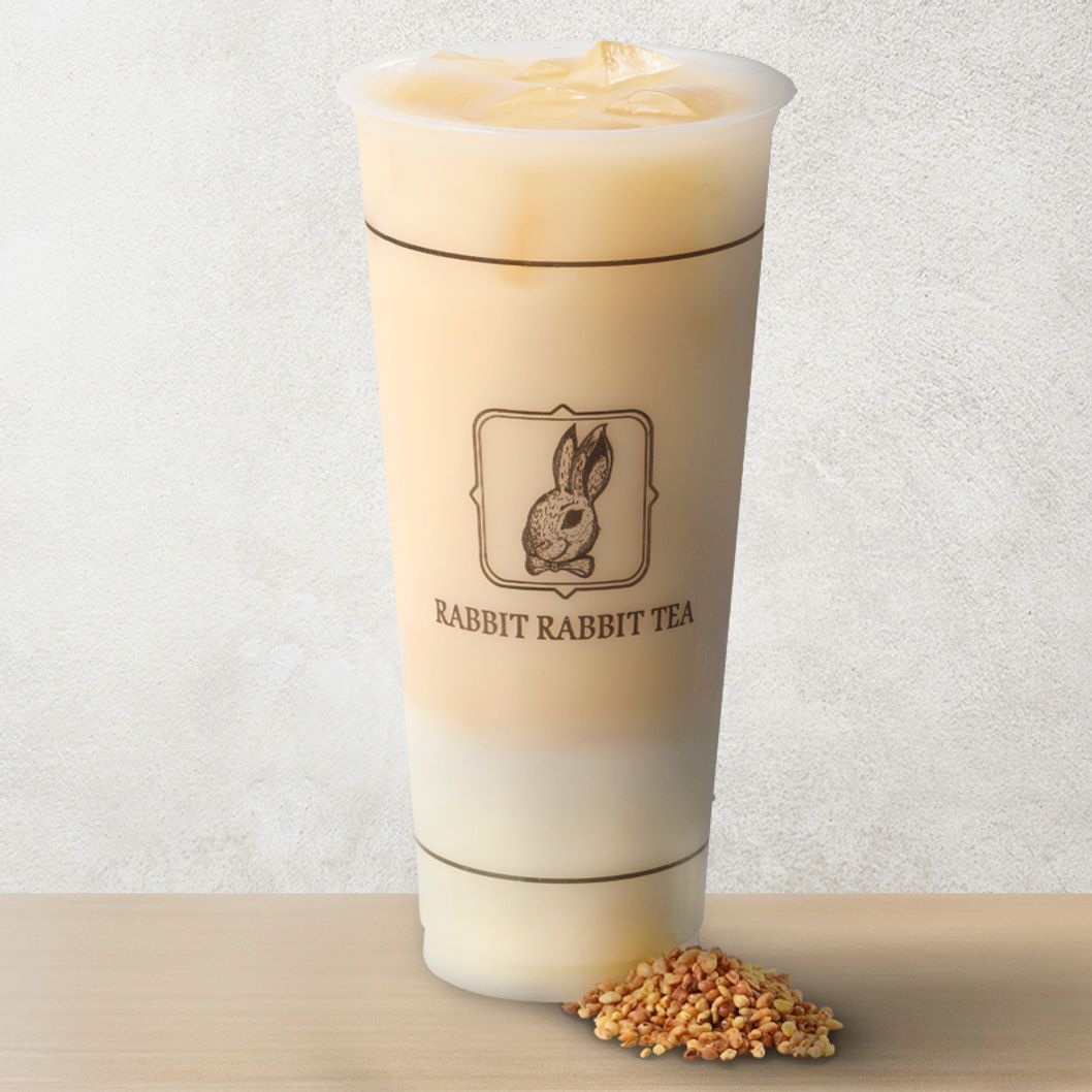 Cream-colored layered drink in a clear cup with a rabbit logo, beside a small pile of granola on a table