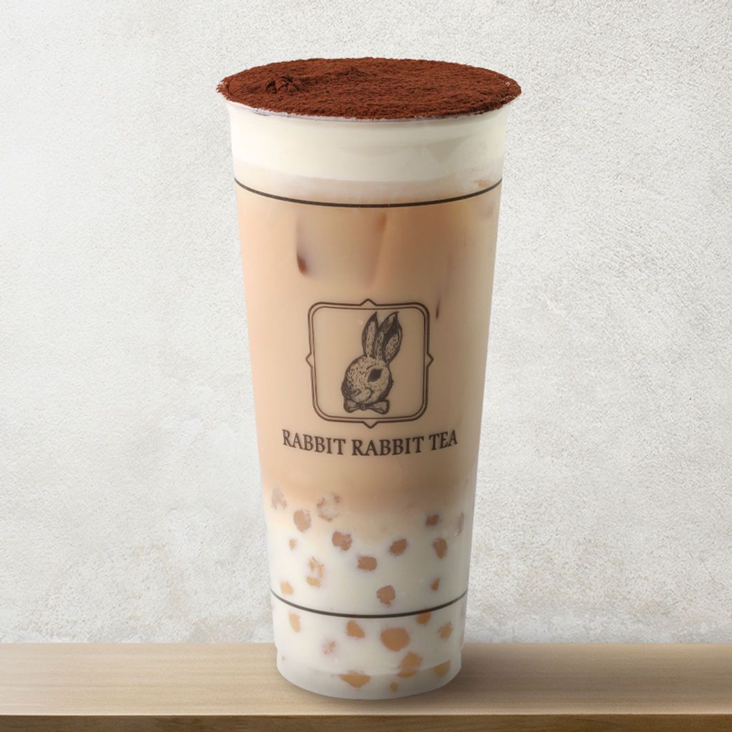 Tall iced milk tea with tapioca pearls and cocoa powder top, in a clear cup with rabbit logo