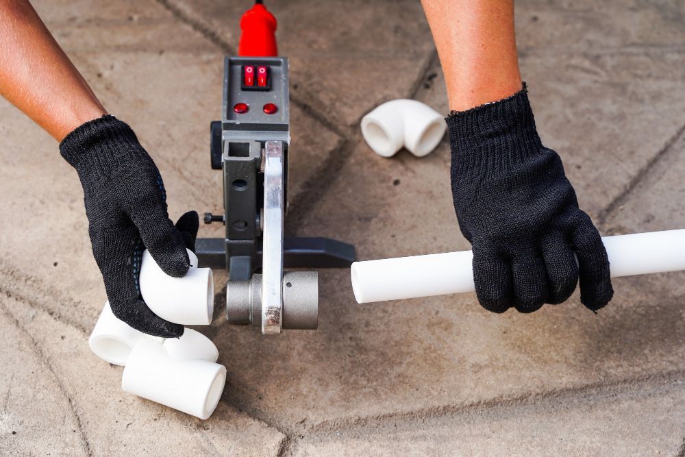 Person using a pipe cutter to cut a white PVC pipe on a tiled floor