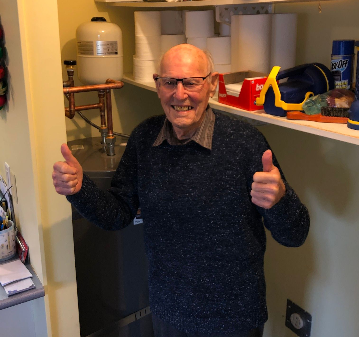 Smiling man indoors giving two thumbs up beside shelves and kitchen items