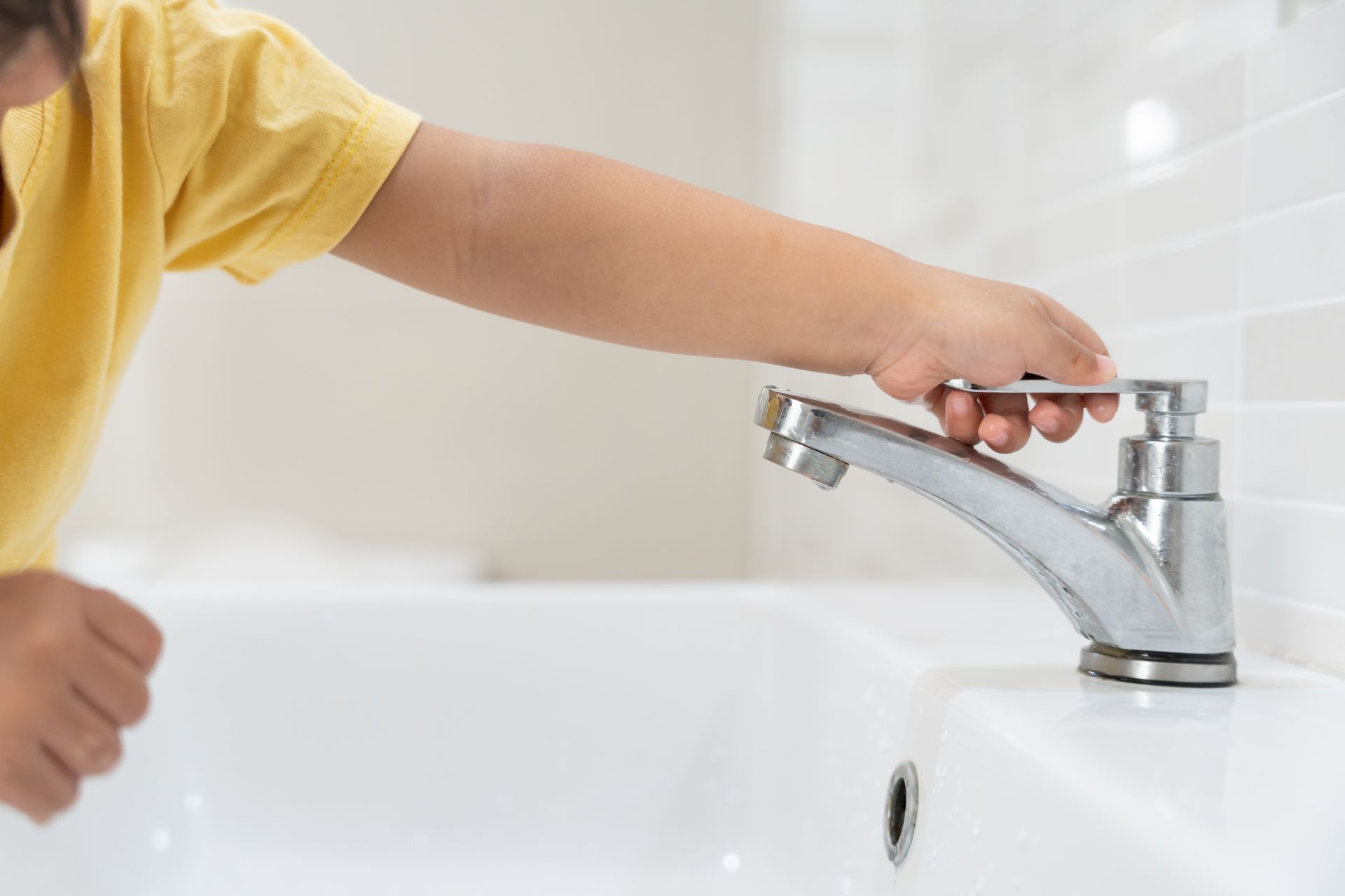 Child’s hand turning a bathroom sink faucet on a white sink