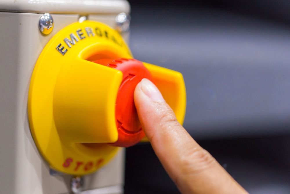 Finger pressing red emergency stop button on yellow panel