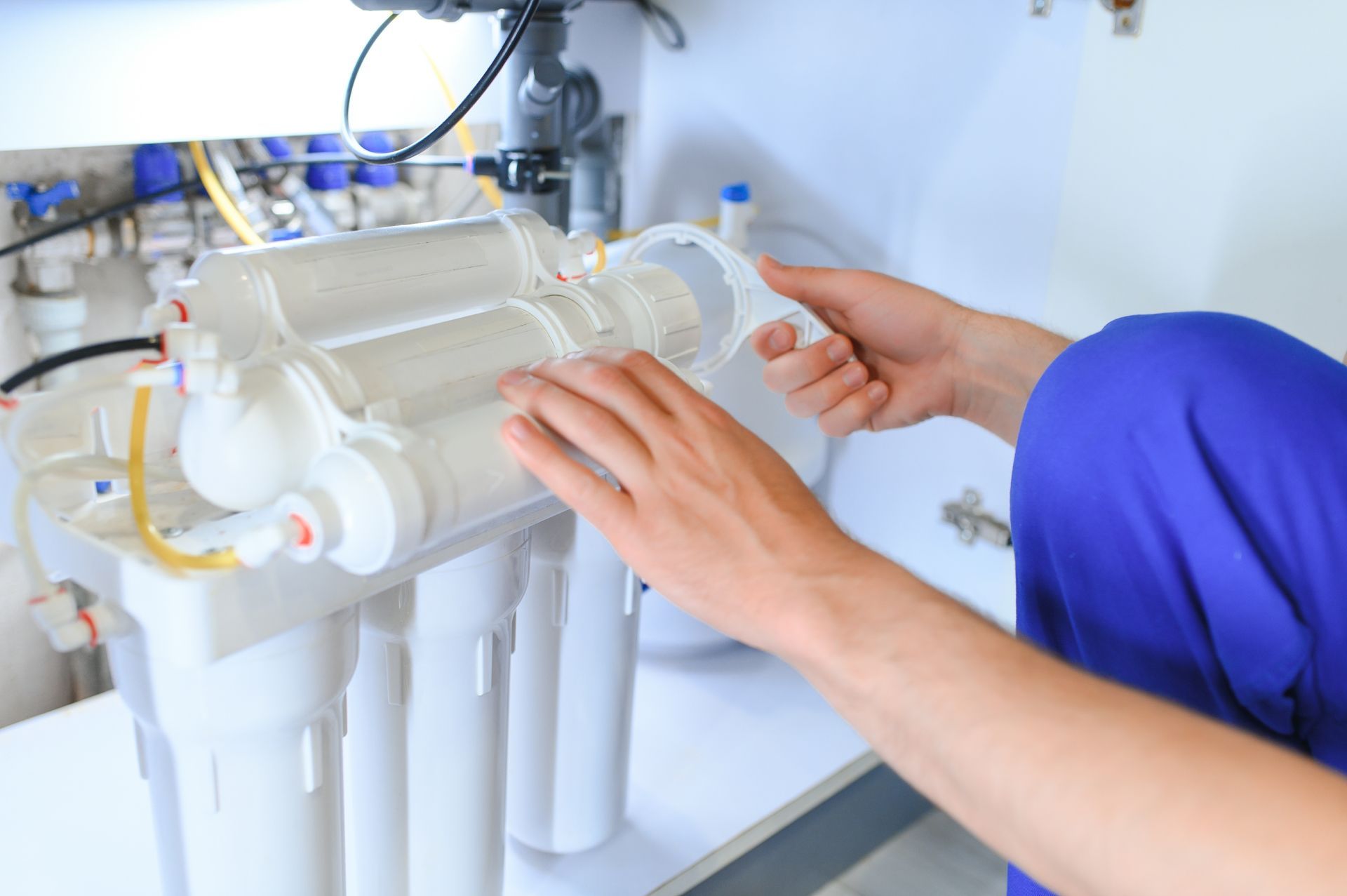 Hands installing a white water filtration unit under a sink
