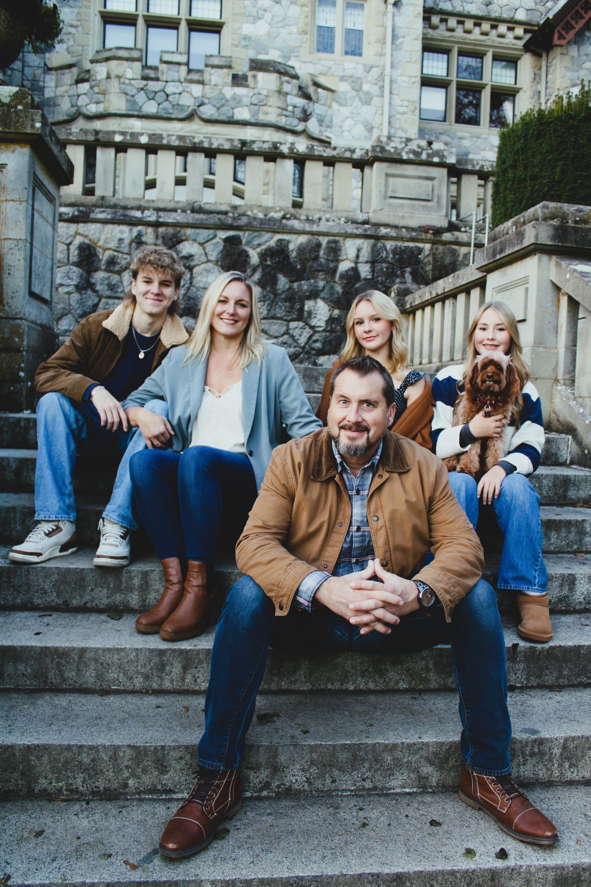 A family is sitting on the steps of a building with a dog.