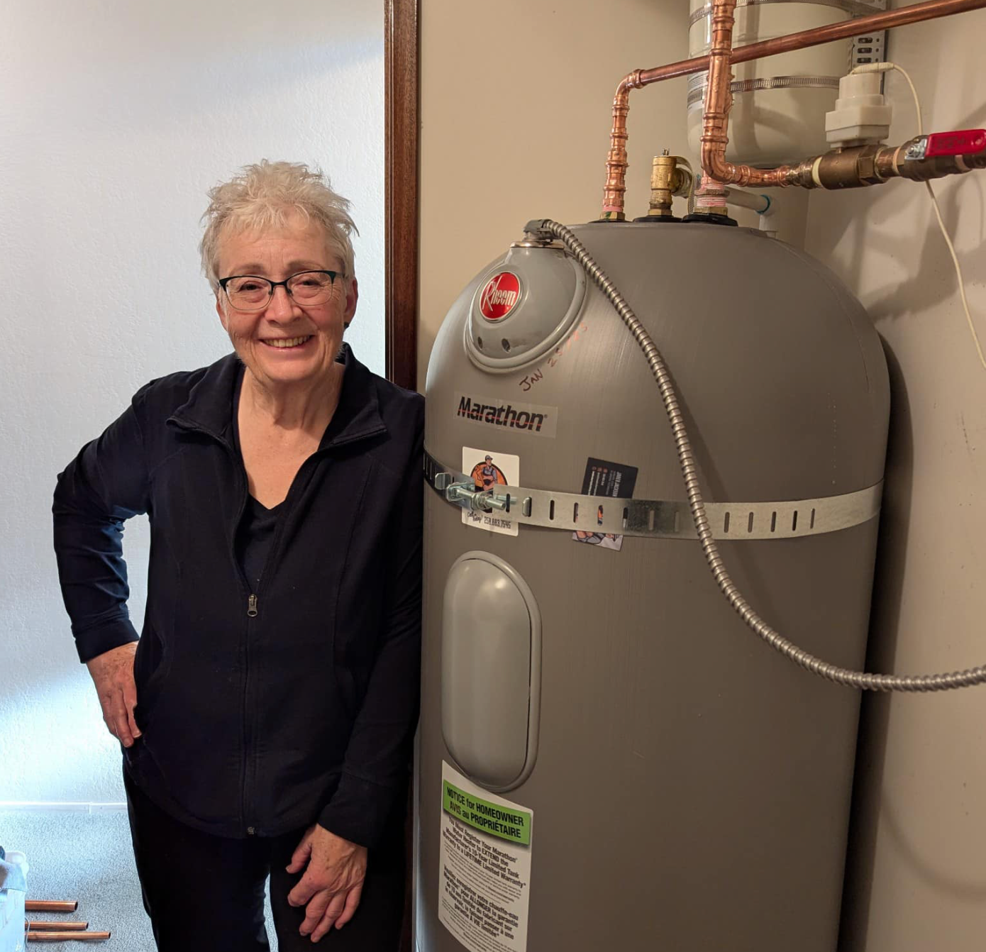 Smiling person standing beside a water heater and exposed pipes in a utility room