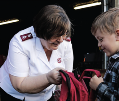 Woman in white shirt helping a child with a red backpack in a dark indoor setting