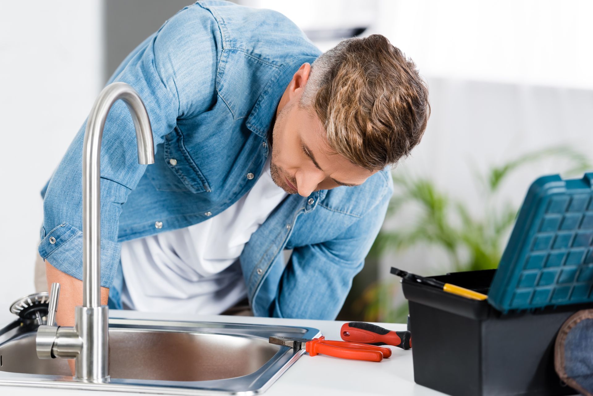 Plumber fixing a kitchen sink with tools beside the faucet