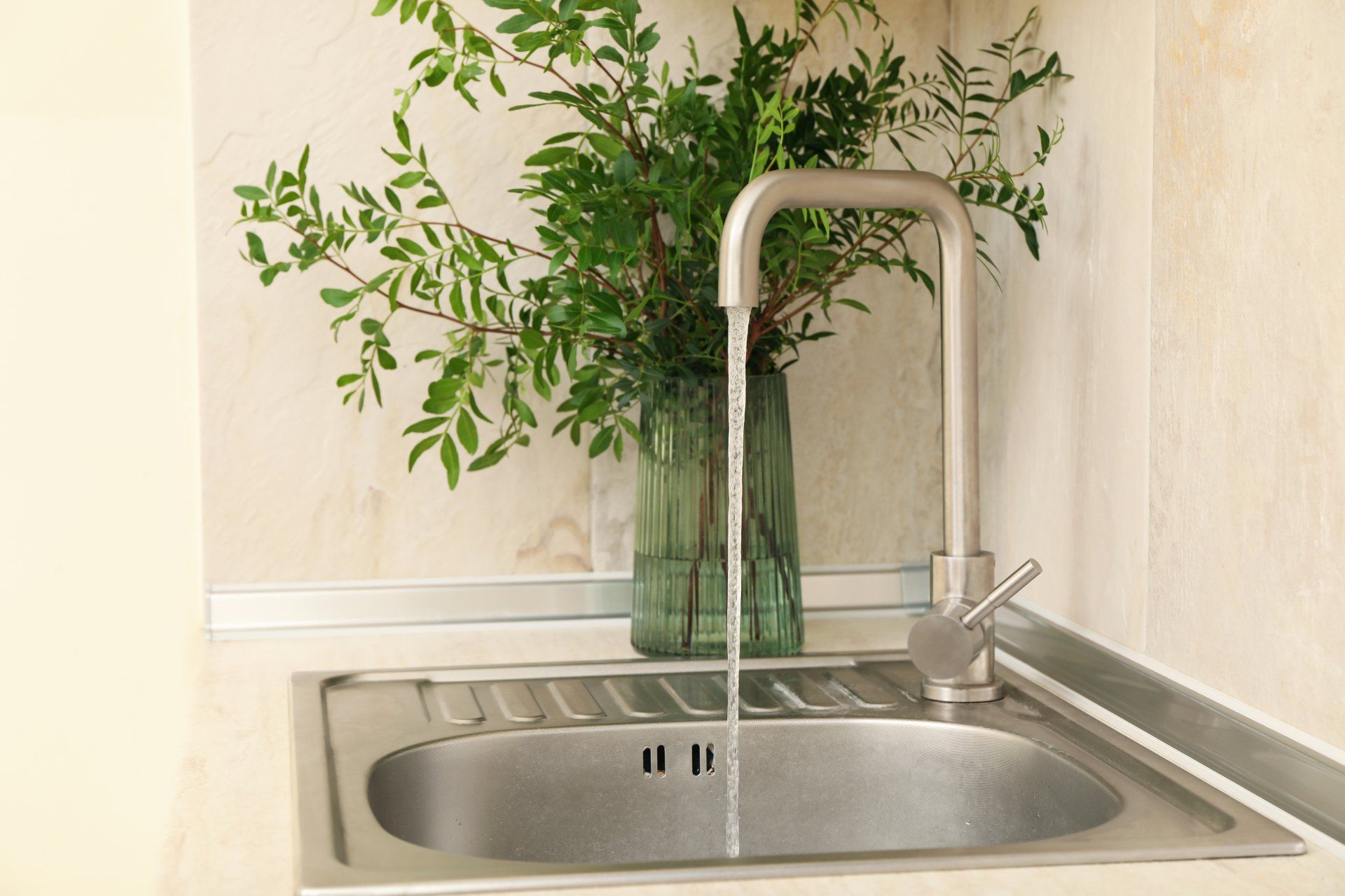 A sink with a vase of flowers in it and water running from the faucet.