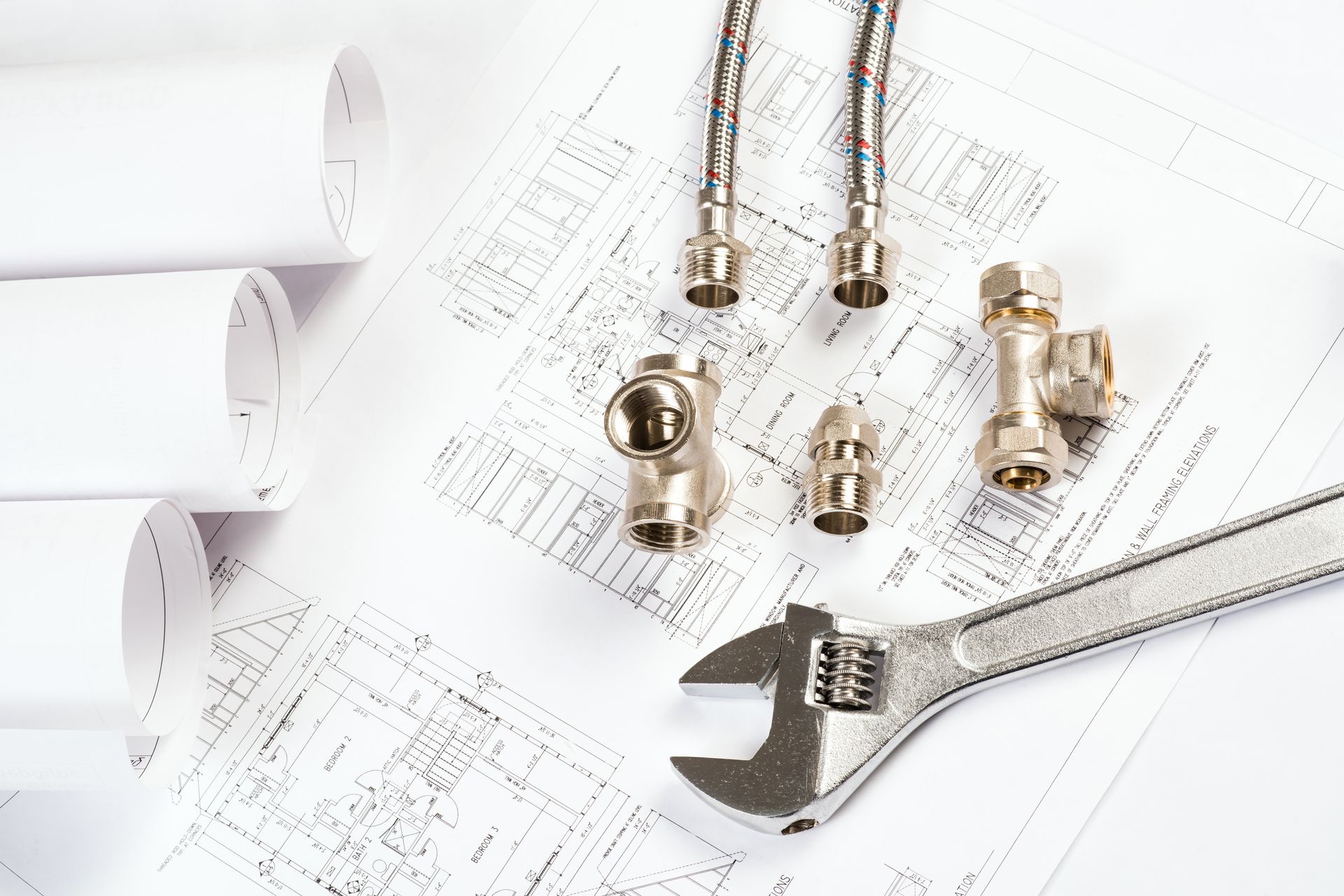 Plumbing tools and fittings on blueprints, including wrenches, valves, and rolled plans