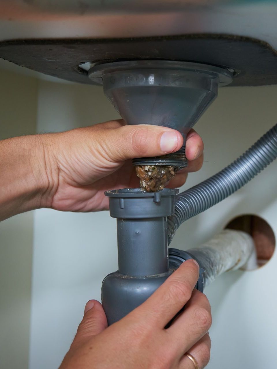 A person is fixing a sink drain in a kitchen.
