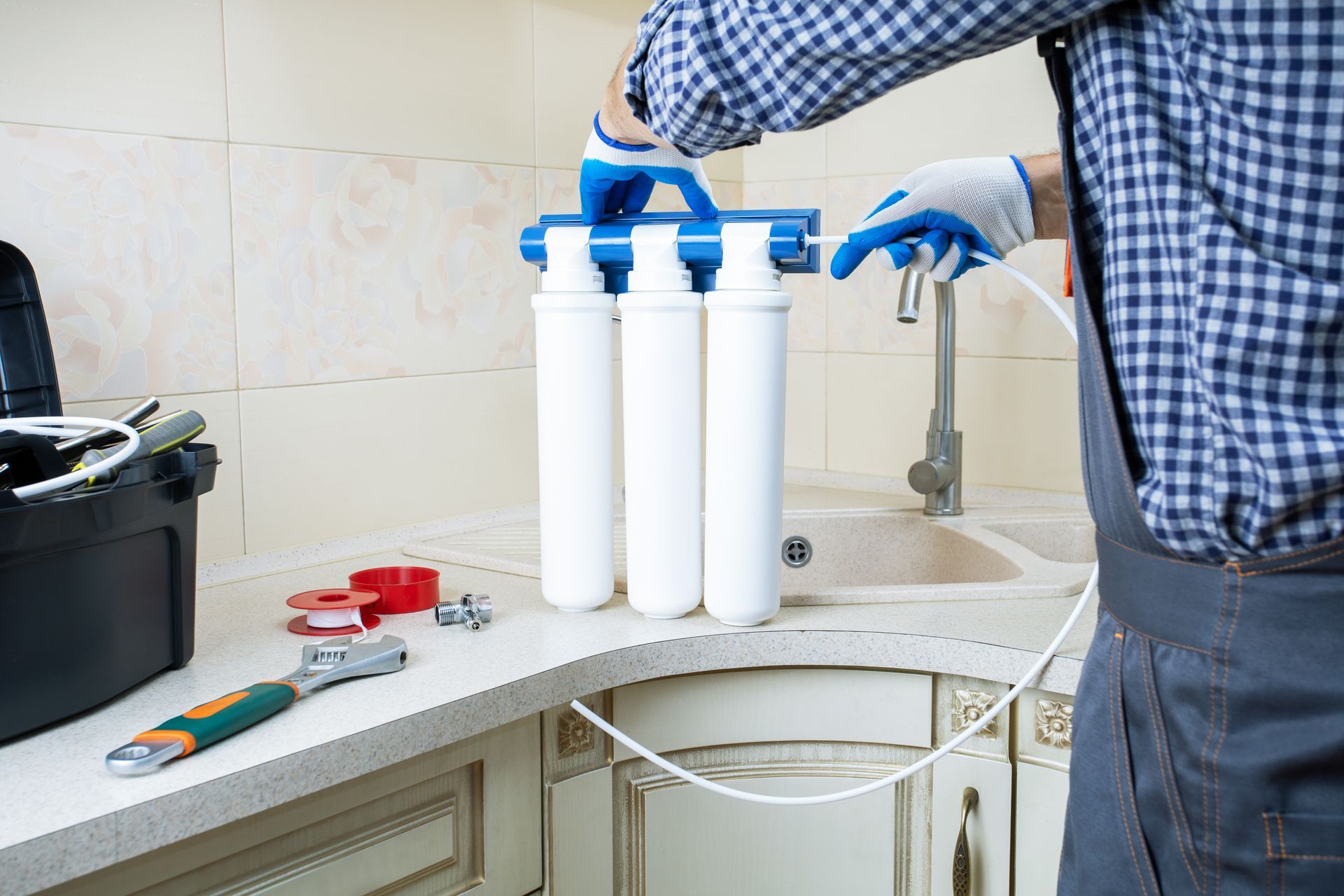 Technician installing white water filter cartridges under a kitchen sink