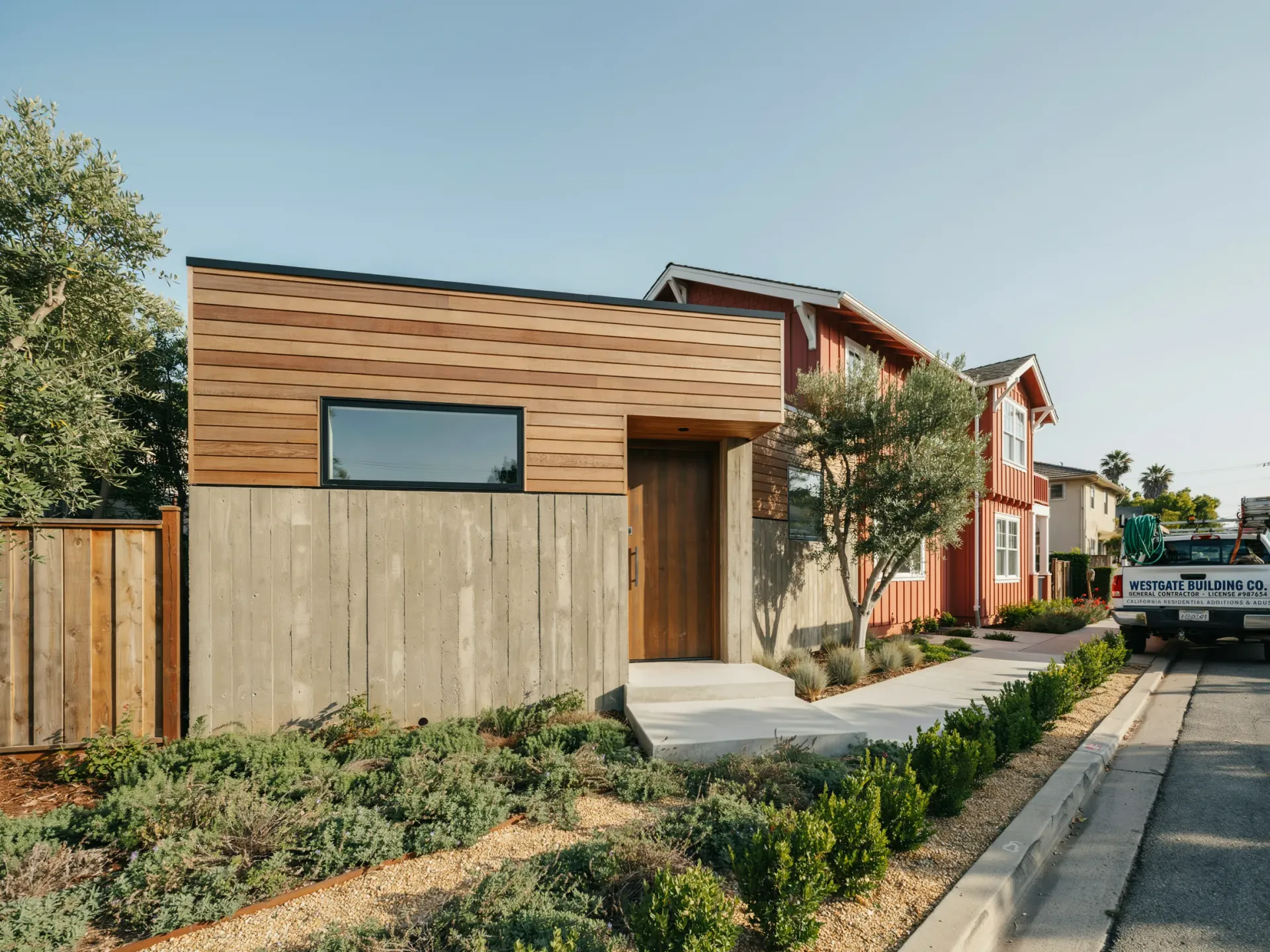 Modern house with wood siding, concrete wall, landscaped front yard, and a sidewalk beside the street.