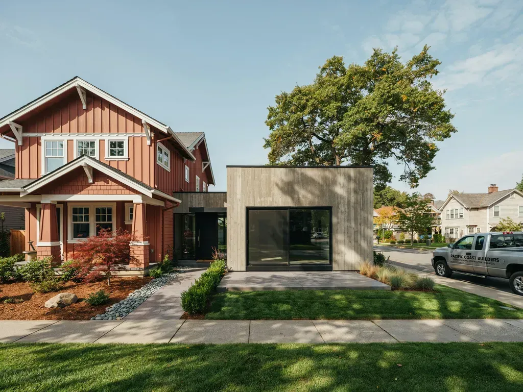 Modern house with a concrete cube facade beside a red two-story home on a sunny residential street