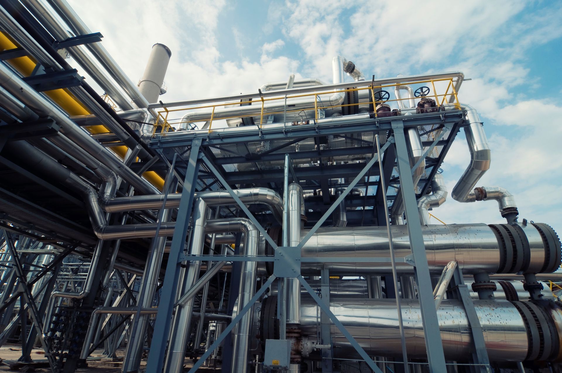 Industrial plant with large metal pipes, steel framework, and processing equipment under a cloudy sky