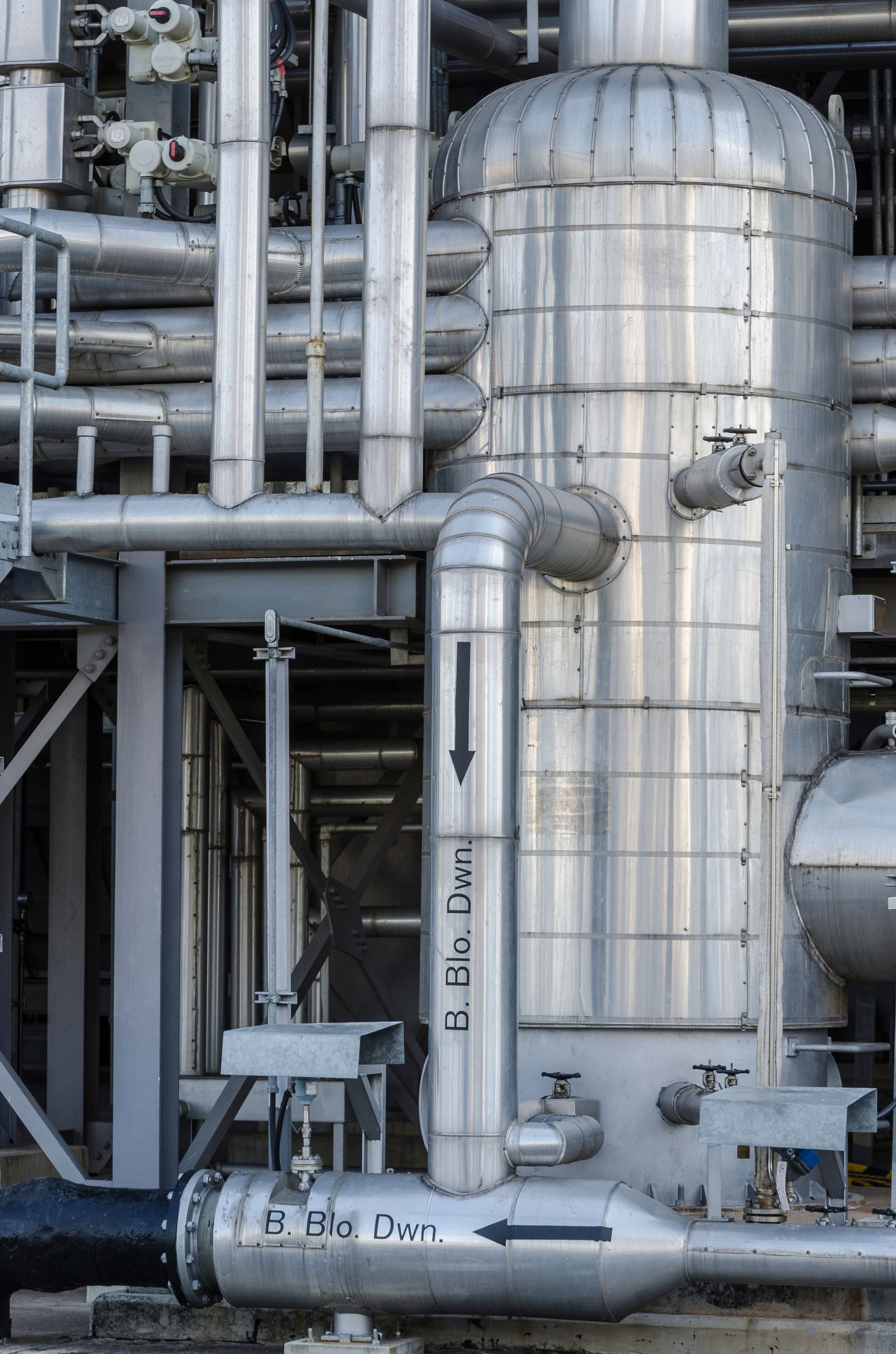 Industrial metal pipes and a silver storage tank in a refinery setting