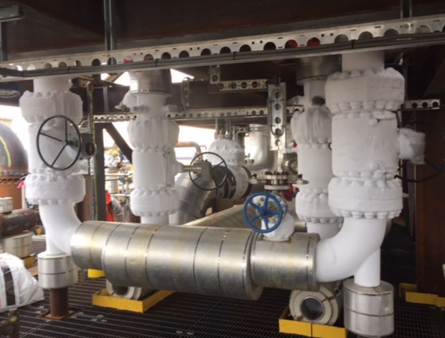 Industrial pipes and valves in a mechanical room, with white insulated piping and blue handwheels.