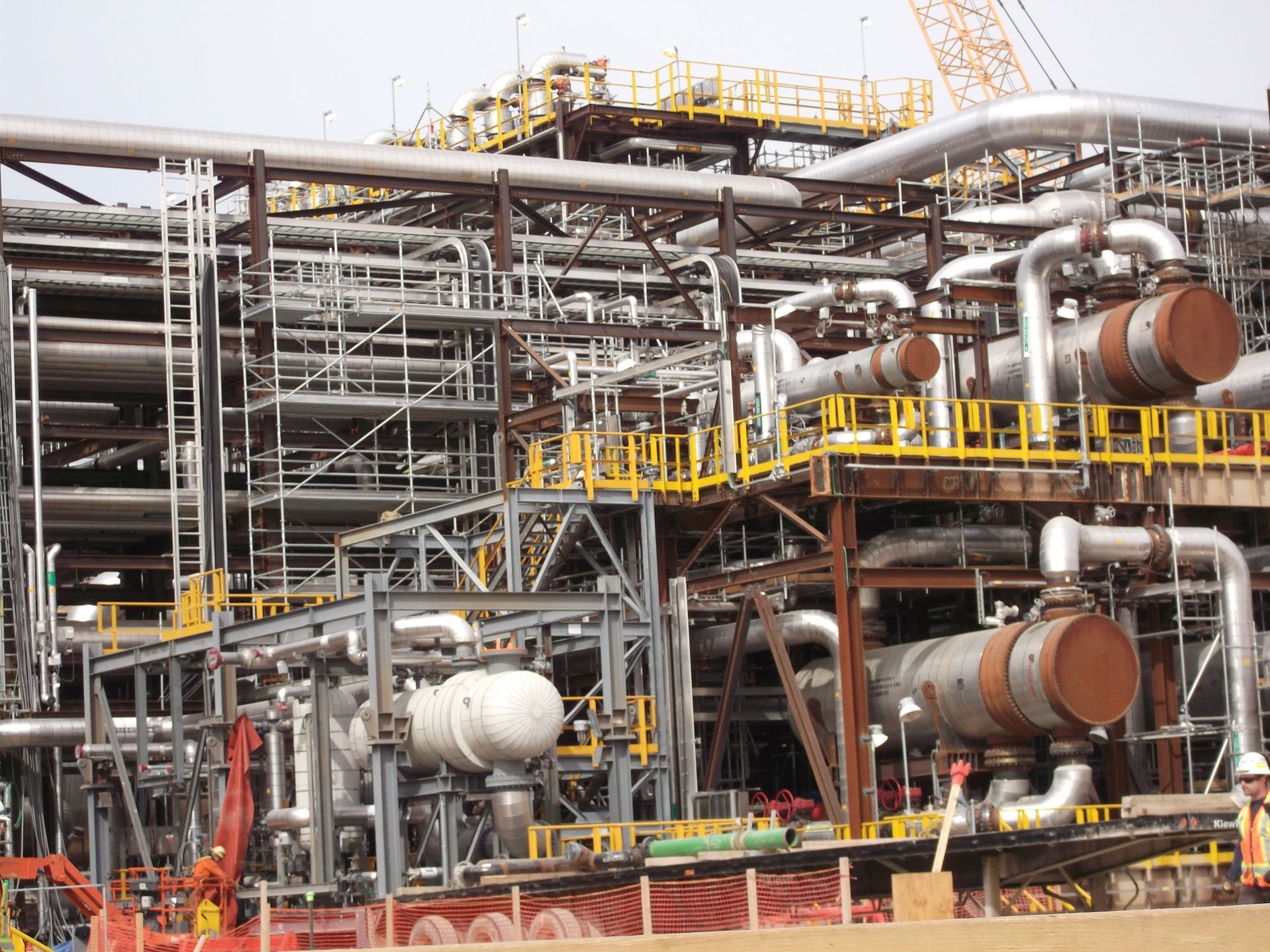 Industrial plant with complex steel scaffolding, pipes, and rust-colored tanks under construction