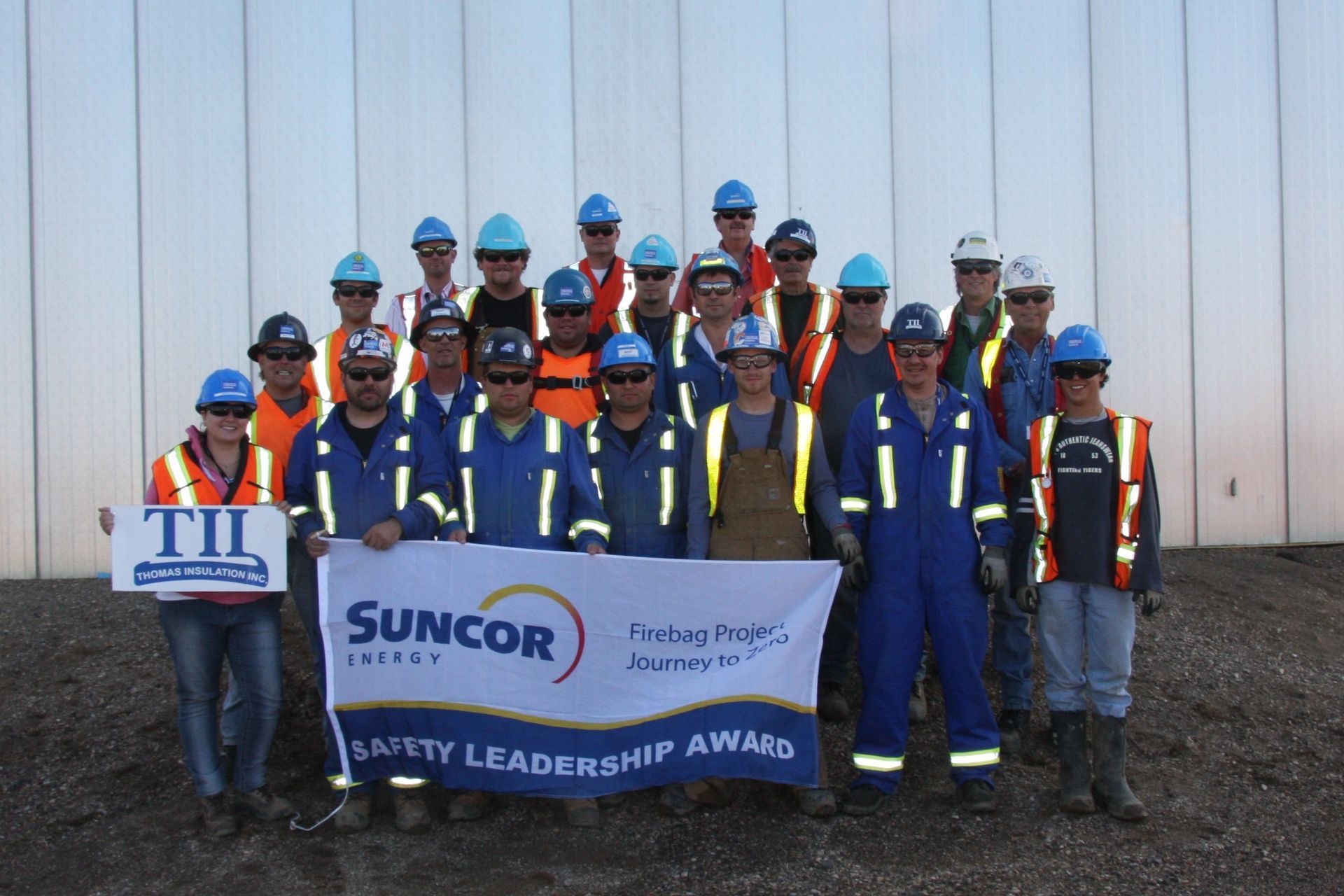 Team of workers in safety gear holding Suncor and TIL banners, standing outdoors for a Safety Leadership Award photo