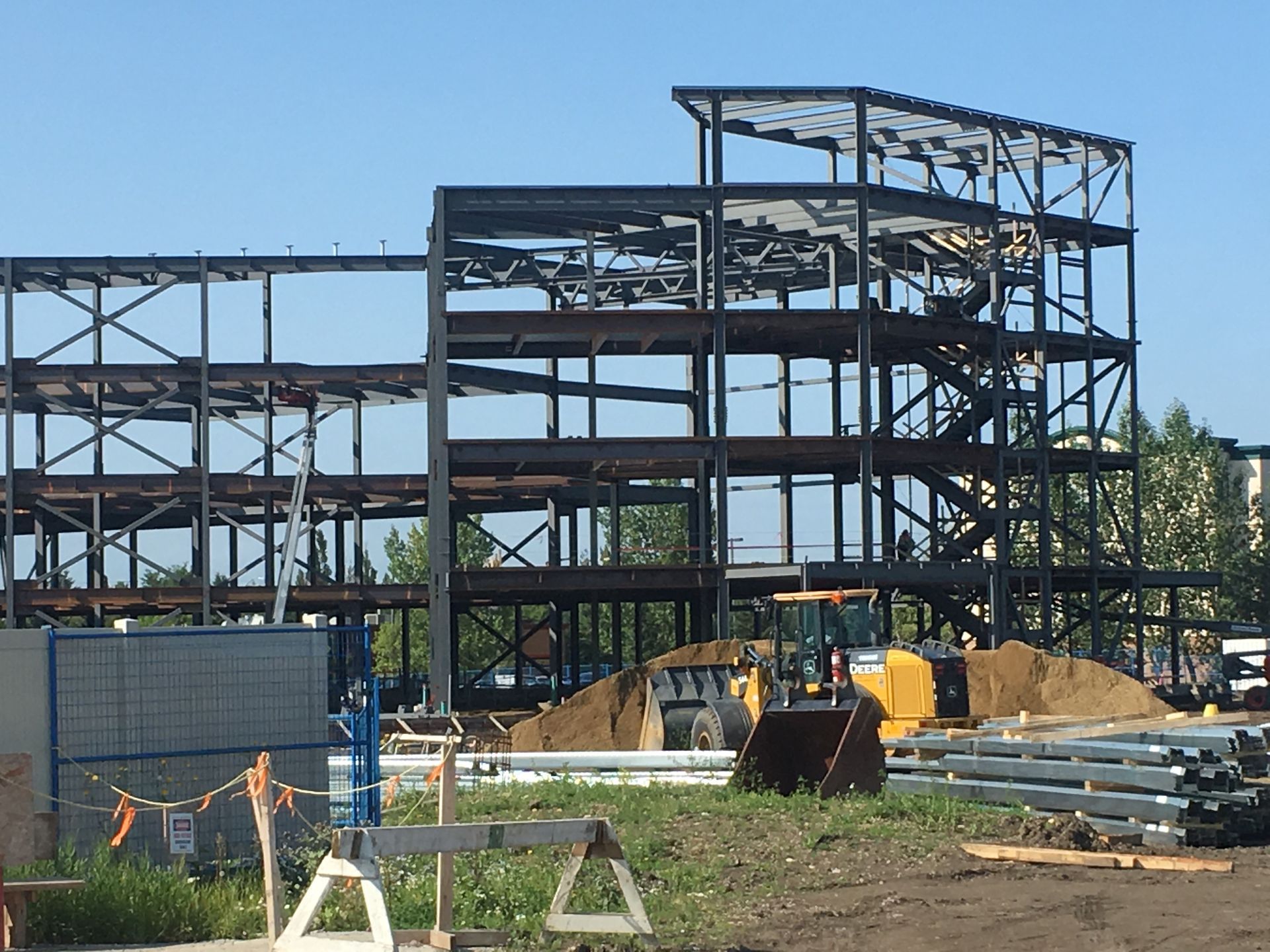 Steel frame construction site with unfinished building, equipment, and materials under a clear sky