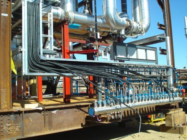 Industrial piping and valves at a refinery, with silver ducts and blue pipes on a metal platform