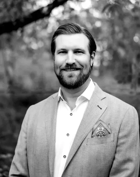 Black-and-white portrait of a smiling man in a blazer standing outdoors.