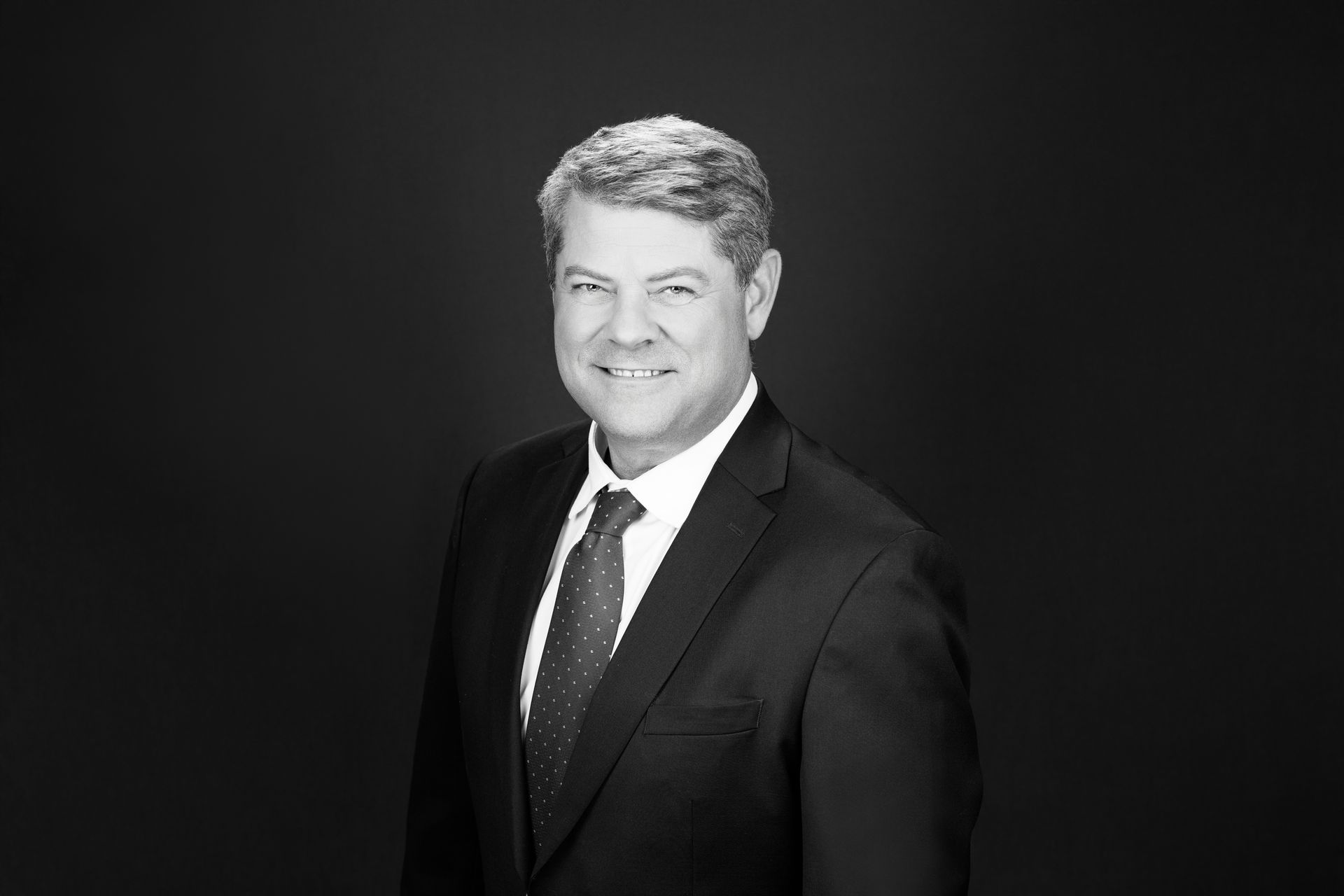 Studio portrait of a man in a dark suit and tie against a black background